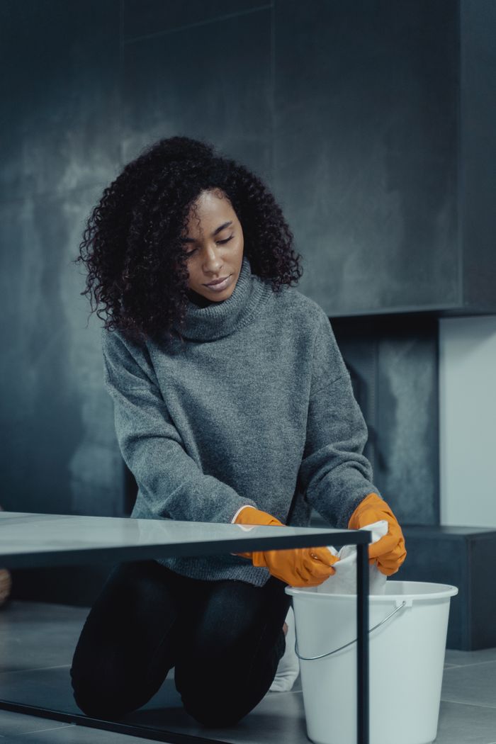 about-img-01 African American woman in gray sweater cleaning with a pail and gloves at home.