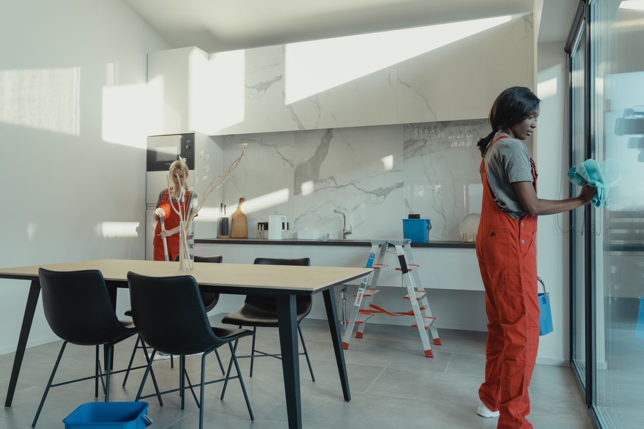 gallery-01 Two women in work clothes cleaning a kitchen with glass doors.